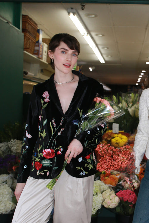 Bethany black silk velvet jacket by Lavanya Coodly, front view with colorful floral embroidery at a flower market